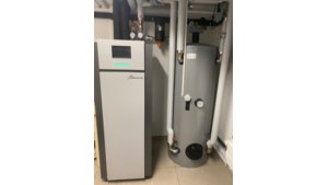 Sole/Wasser-Wärmepumpe KLIMT von bösch in einem Heizungsraum, neben einem großen grauen Warmwasserspeicher. Die Wärmepumpe ist mit einem digitalen Display ausgestattet und verbunden mit mehreren Rohrleitungen, Ventilen und Manometern zur Steuerung der Temperatur und Wasserzirkulation. | © Walter Bösch GmbH & Co KG