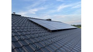 Reihe von dunklen Photovoltaikmodulen auf einem grauen Dachziegel, mit einem leicht bewölkten blauen Himmel im Hintergrund. Die PV-Module sind effizient angeordnet, um maximale Sonneneinstrahlung zu nutzen, und bieten eine umweltfreundliche Energielösung. | © Walter Bösch GmbH & Co KG